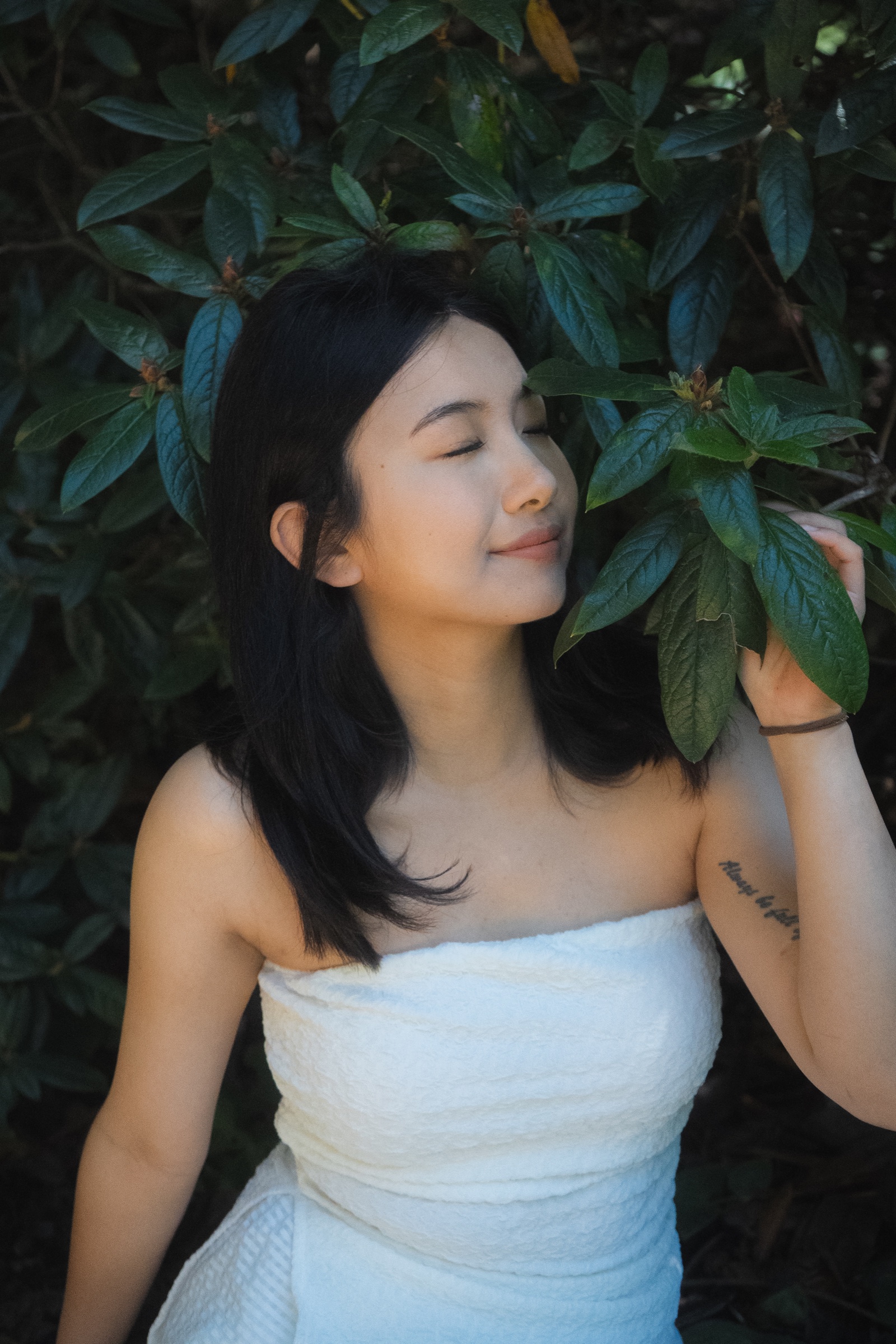 Close portrait of a woman in a white dress gently holding a leafy branch with her eyes closed.