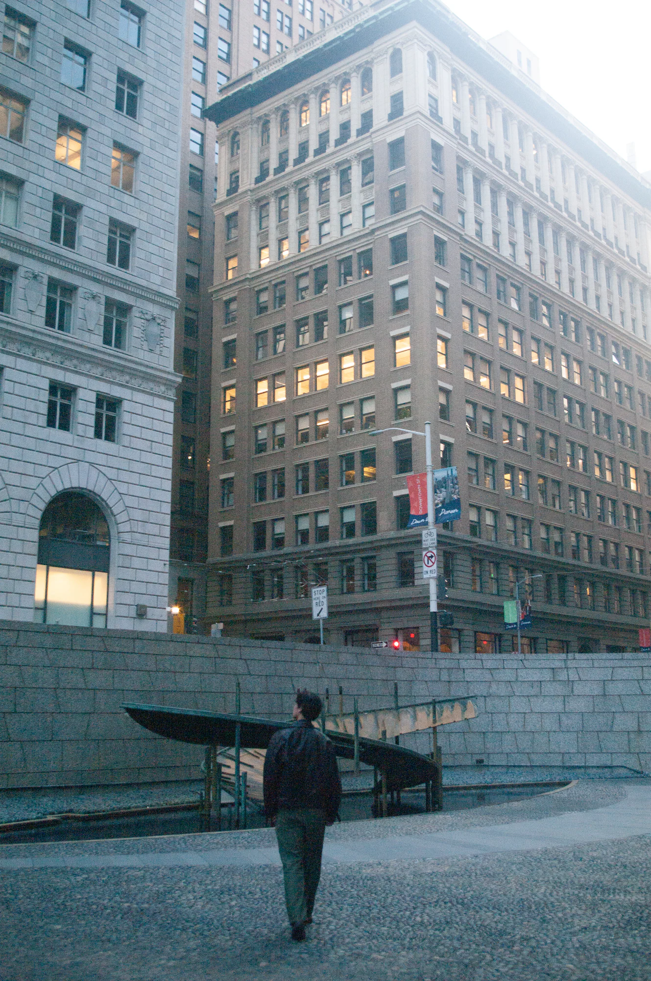 Figure seen from behind beneath tall downtown buildings at dusk.