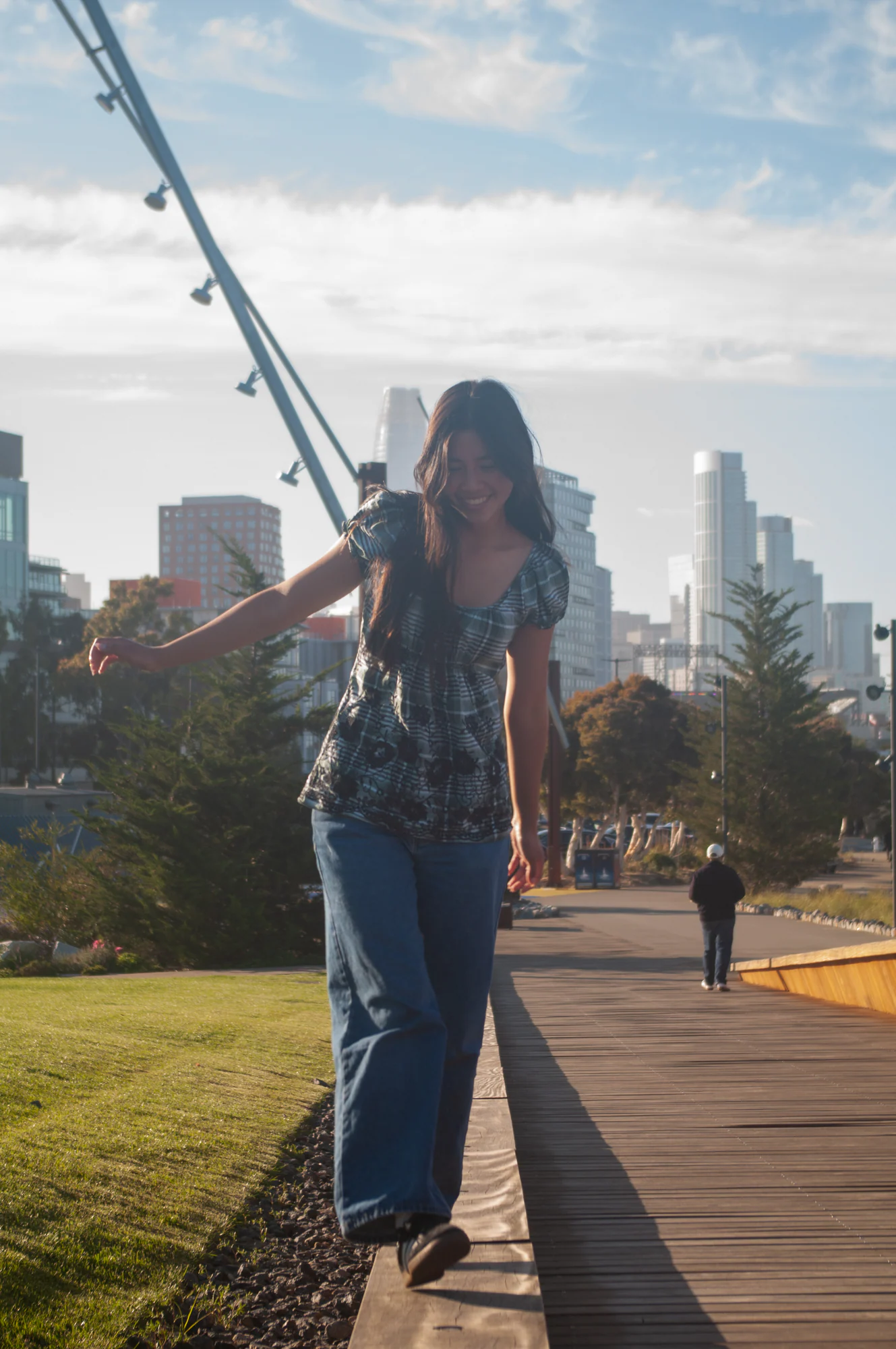 Woman walking along a waterfront path with the San Francisco skyline behind her.