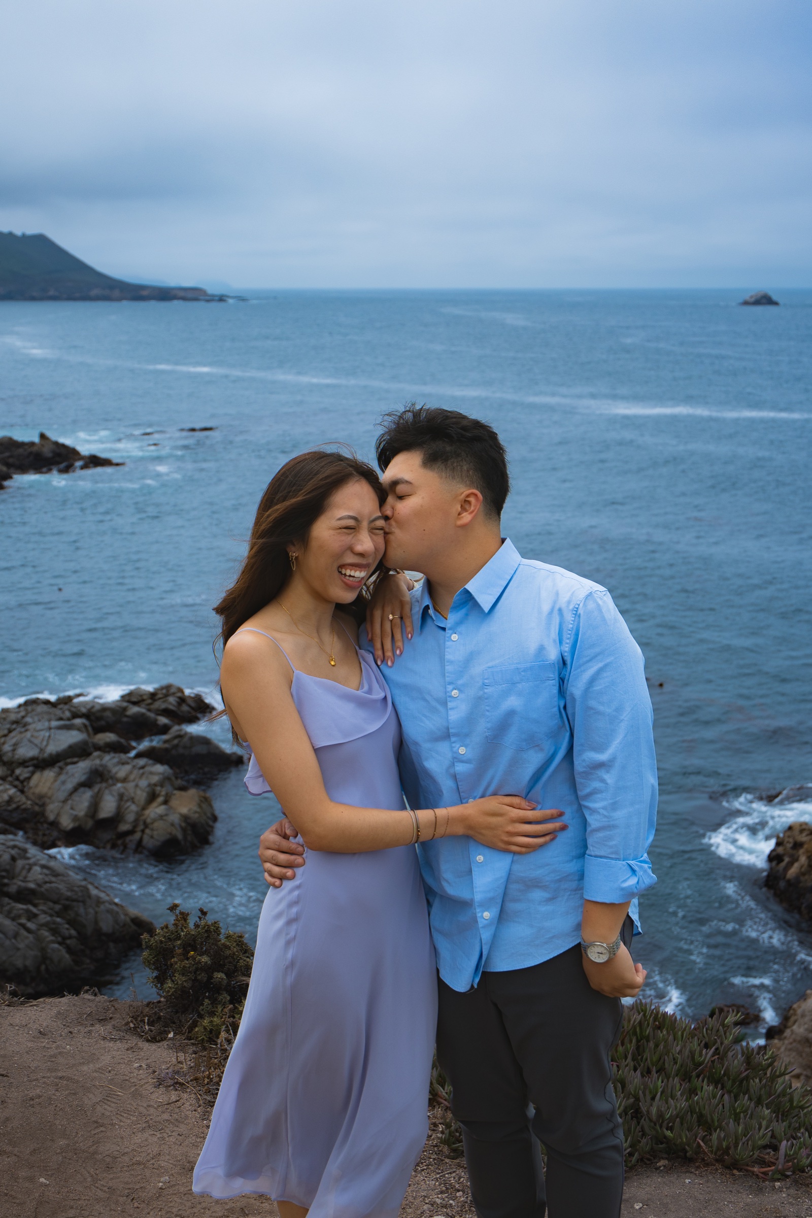 Couple embracing on a rocky California coastline above the ocean.
