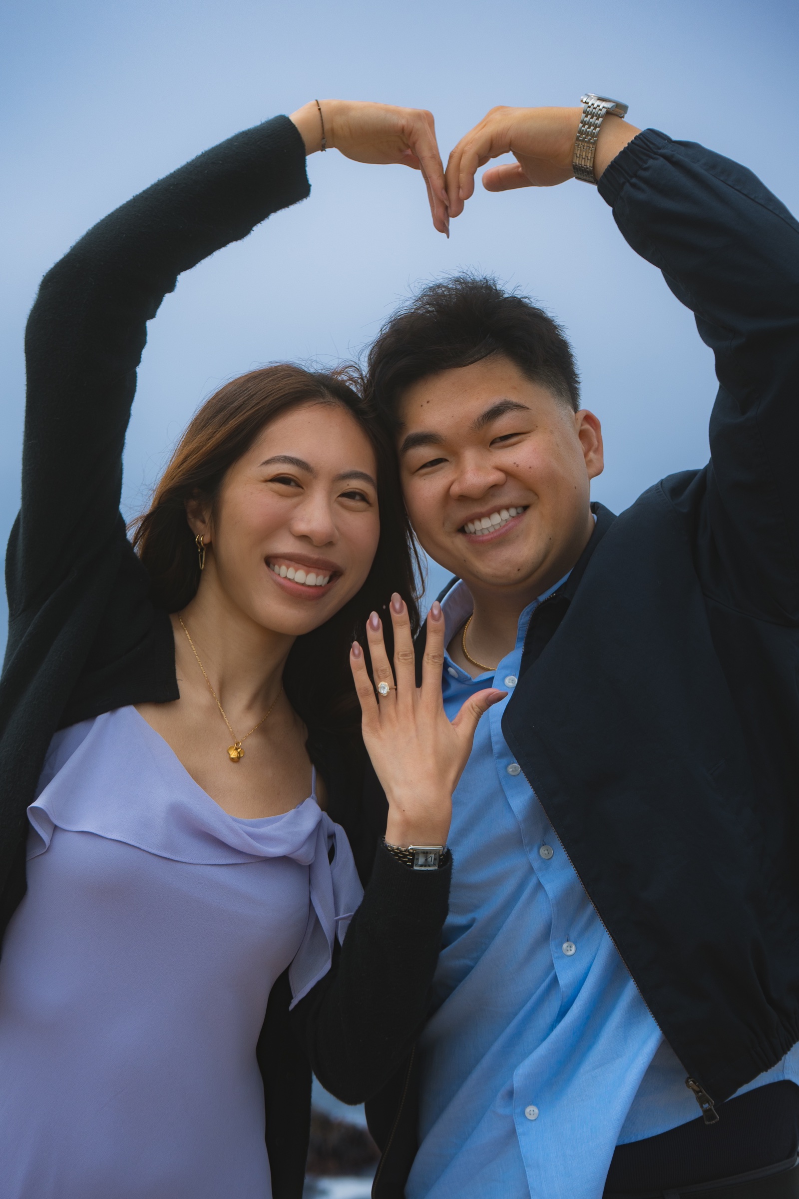 Joyful close portrait of an engaged couple holding their hands in a heart shape.