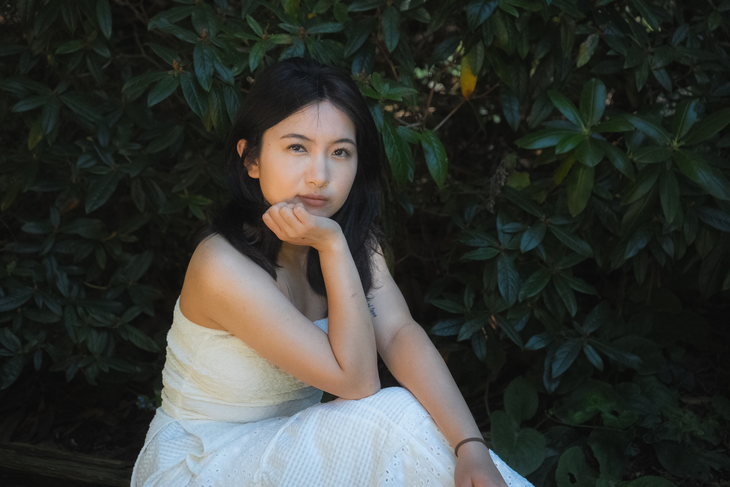 Seated portrait of a woman in a white dress framed by dark green leaves.