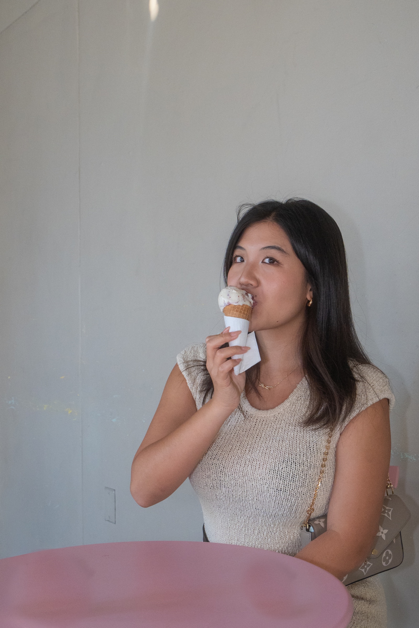 Indoor portrait of a woman holding an ice cream cone beside a softly colored wall.