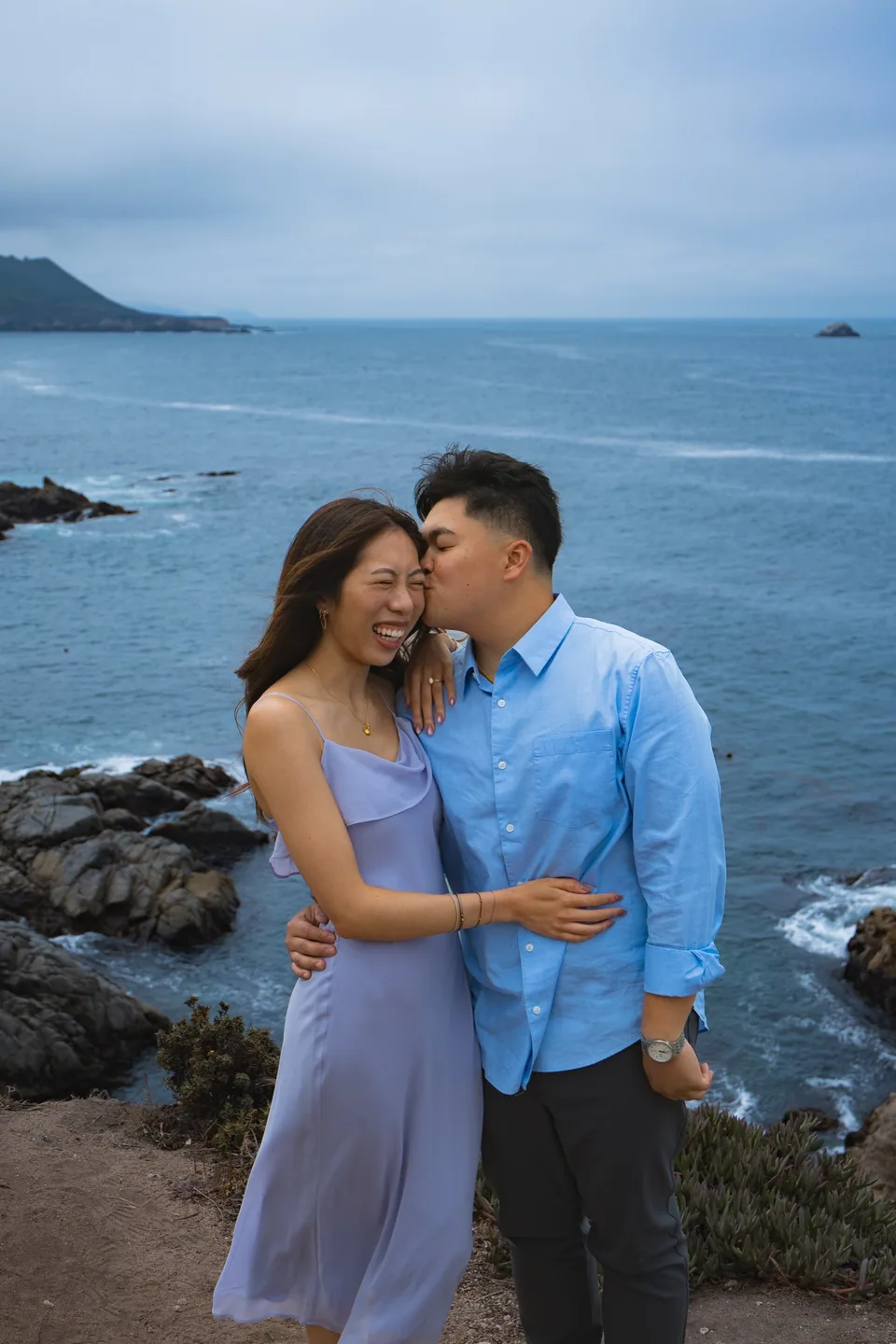 Couple embracing on a rocky California coastline.