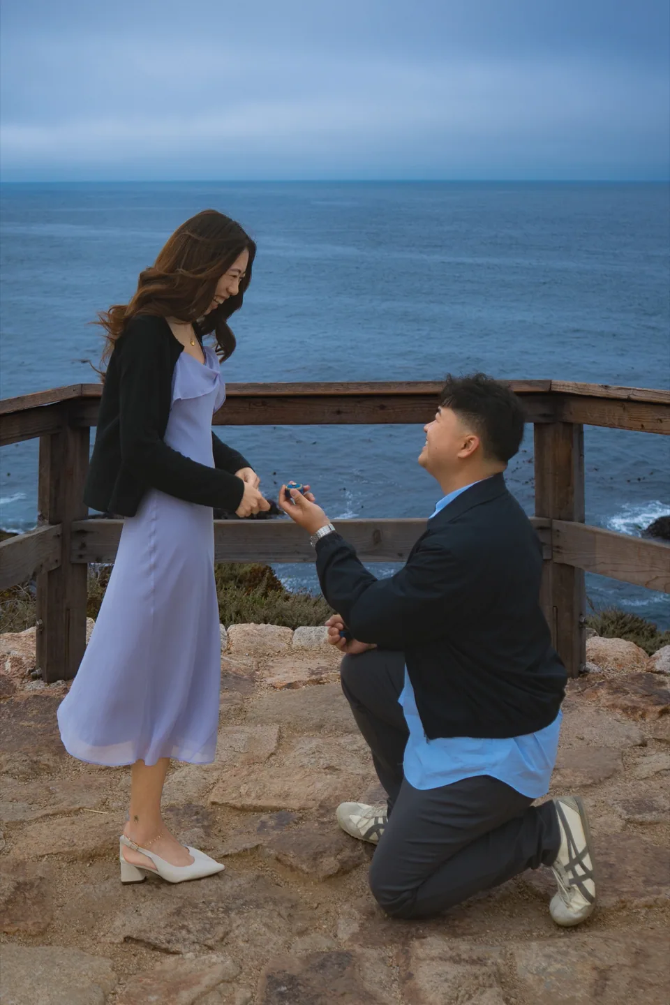 A man proposing to his partner on a coastal overlook above the ocean.