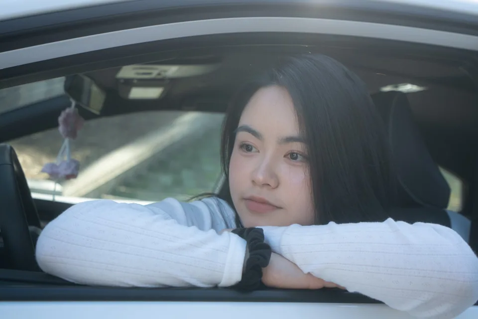 Portrait of Vivan Chen resting her arms on an open car window in soft afternoon light.