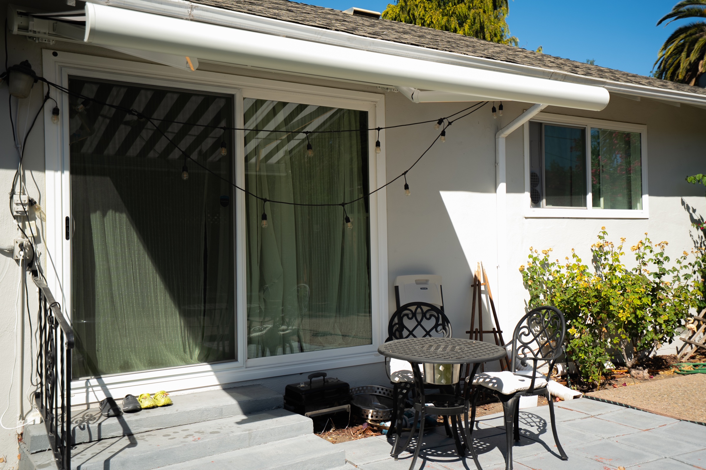 Sunlit residential patio with sliding glass doors, outdoor seating, and a retractable awning.