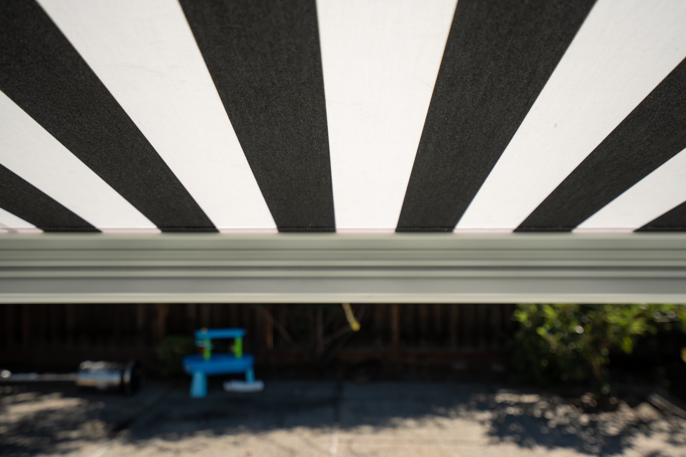 Close view beneath a black-and-white striped awning with the backyard softly out of focus.