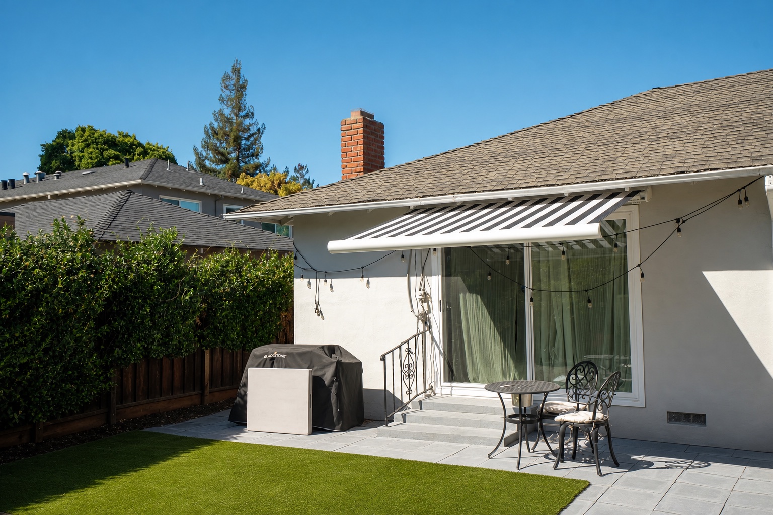 Wide exterior view of a landscaped backyard and patio shaded by a black-and-white retractable awning.