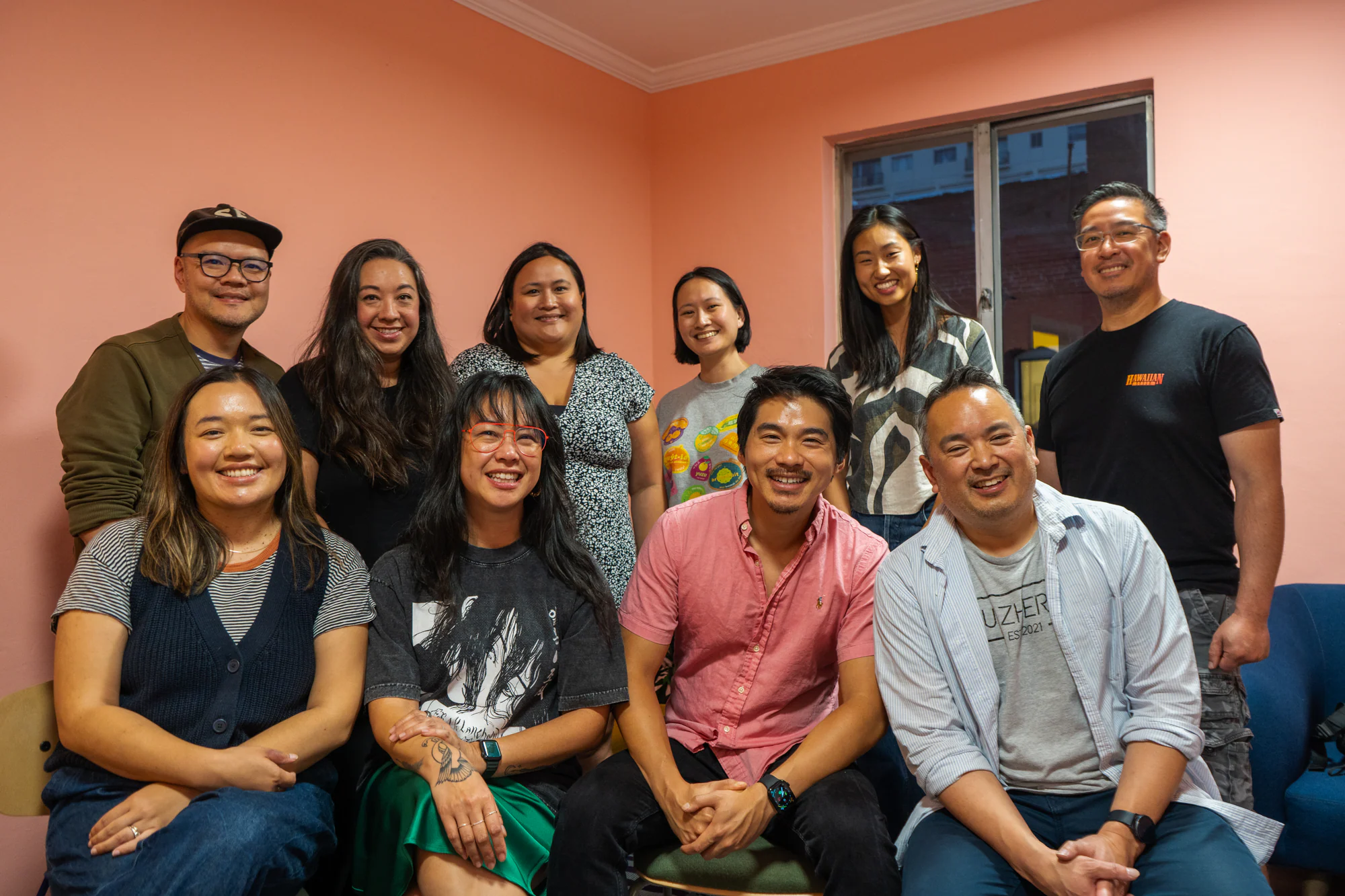 Ten adults posing in two rows against coral-colored walls at an indoor gathering.