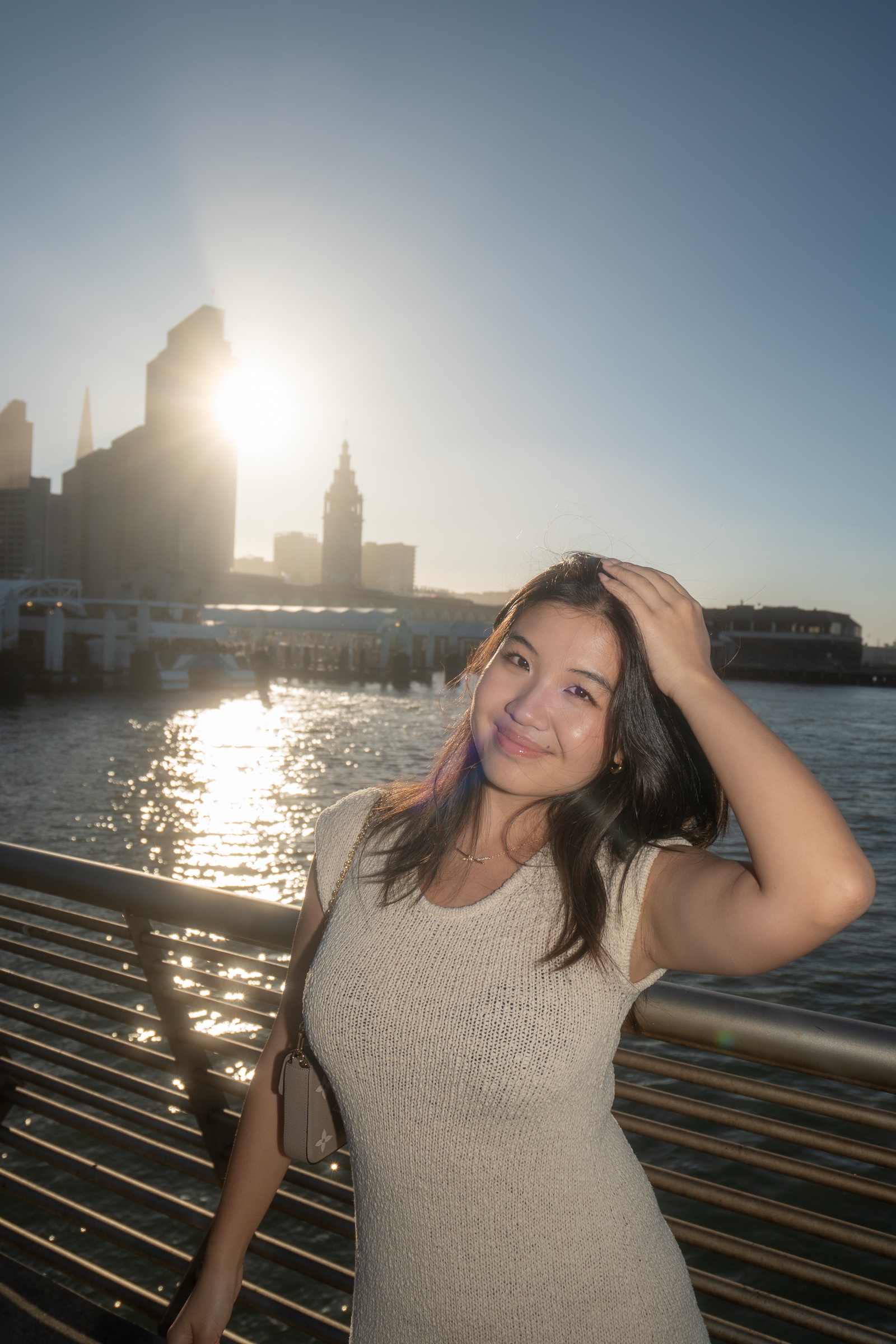 Sunlit waterfront portrait of a woman with the San Francisco skyline glowing behind her.